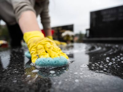 Headstone cleaning on cemetery. Professional in yellow gloves cleans the marble grave, scrubbing with sponge and water. Tombstone preparation for All Saints Day on November 1st